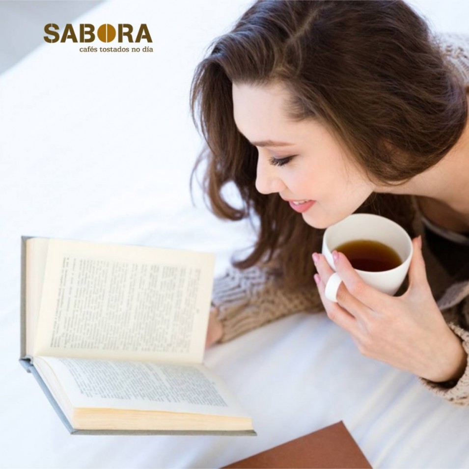 Rapaza lendo un libro cun gran café na casa